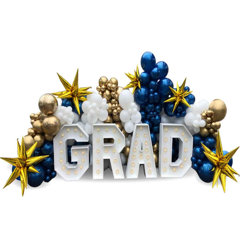 4 Light up marquee letters spelling GRAD nested in a balloon wall in blue, gold and white. Salem Oregon balloon decor and marquee letters rental