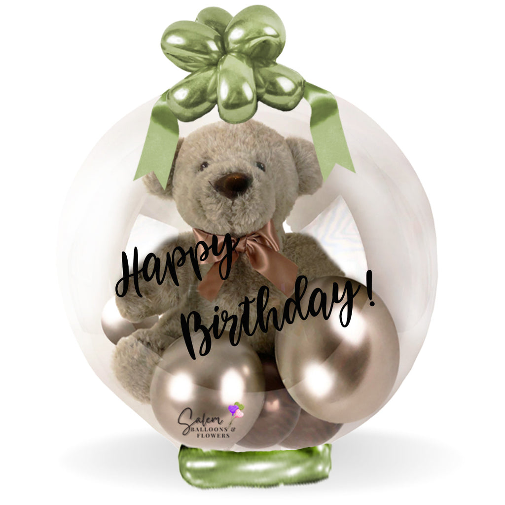 Beige teddy bear in a clear bubble balloon decorated with ribbon and a 