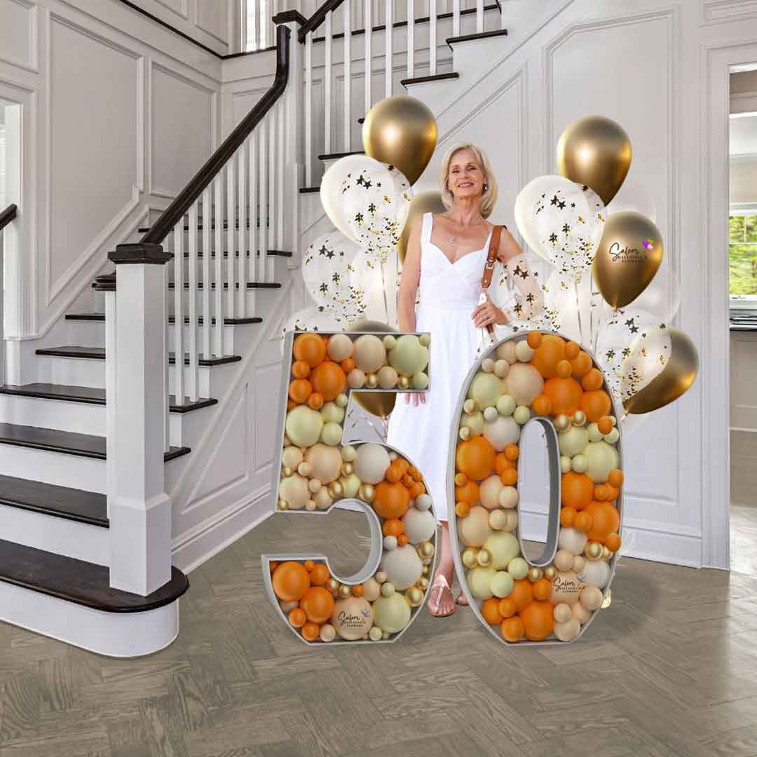 A lady posing for a picture behind  Number 50 of  3 ft tall Mosaic balloon number in orange, blush and pastel yellow. Balloon delivery in Salem Oregon
