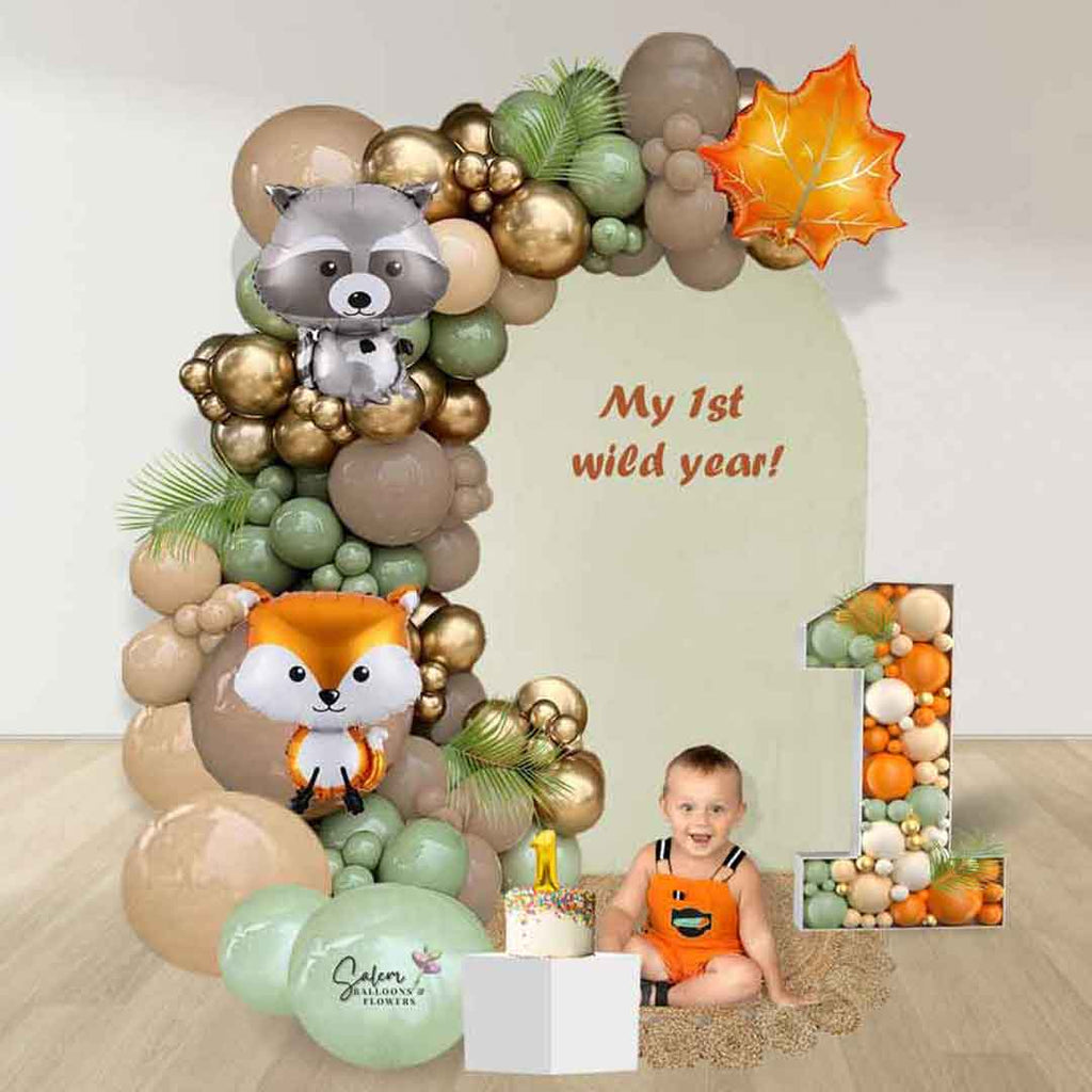 A balloon display in a woodland theme with a balloon garland, a personalized panel, cake stand, rug and number 1 mosaic balloon number. Delivery in Salem Oregon and nearby cities.