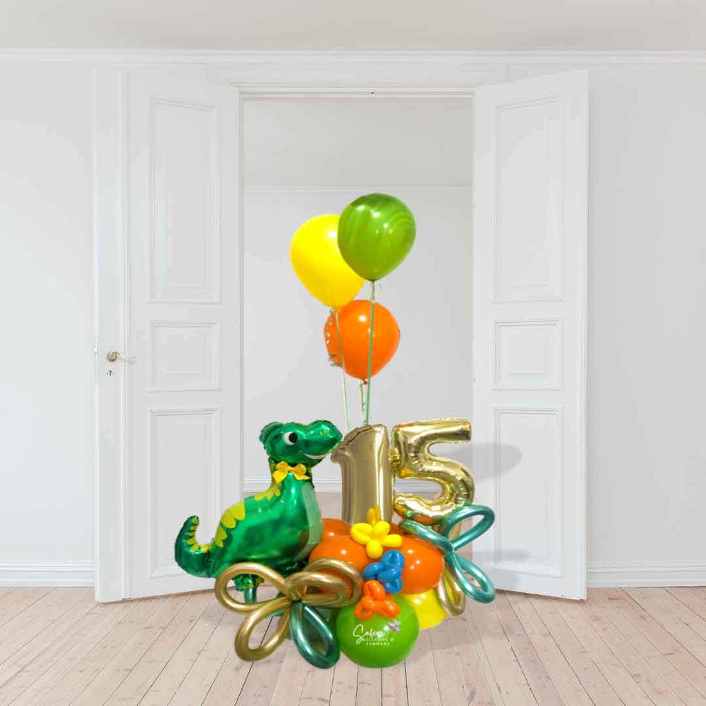 Dinosaur themed number balloon bouquet with a cute dinosaur balloon, in a kiwi green, orange and yellow color palette standing in front of a white door. Salem Oregon balloon delivery.