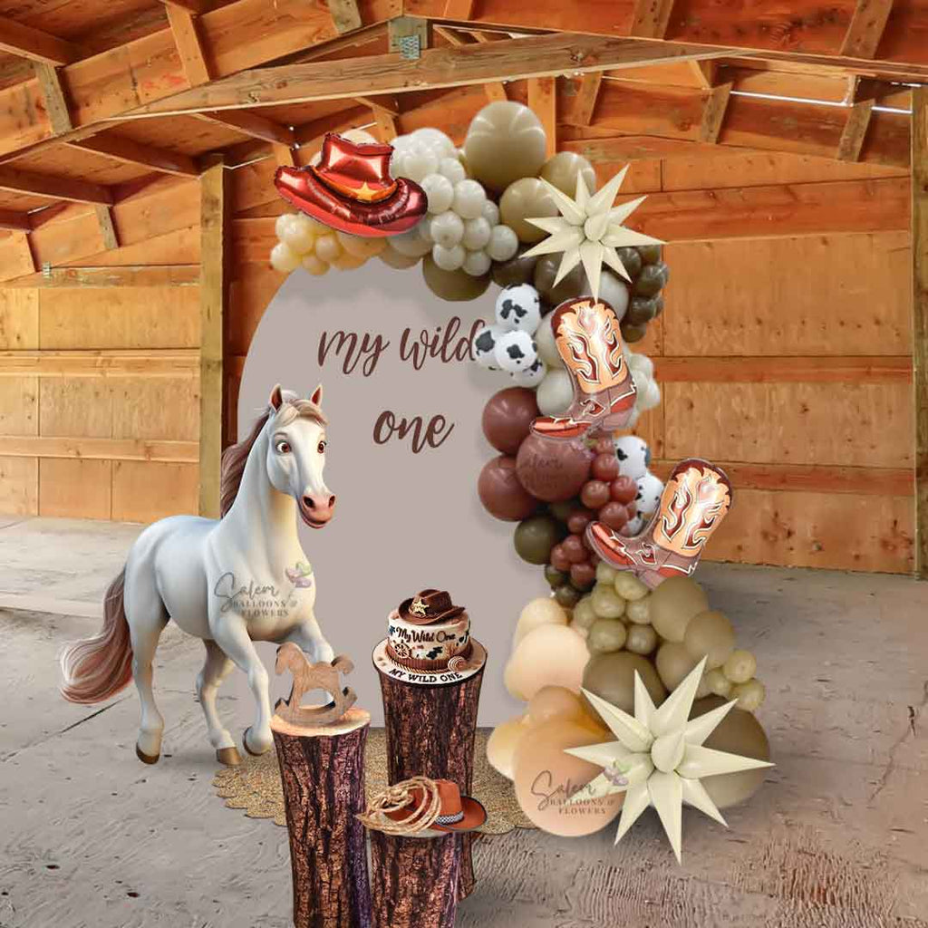 A barn with a Wild West celebration! This setup features a stunning Chiara panel adorned with a gorgeous organic balloon garland, accented with cowboy hats, boots, and spiky stars for the perfect Western touch. Rustic, trunk-like cake stands complement the theme, while an adorable horse cutout adds a charming focal point. To complete the look, a round jute rug ties everything together, creating the ultimate cowboy-inspired scene.  
Oregon.