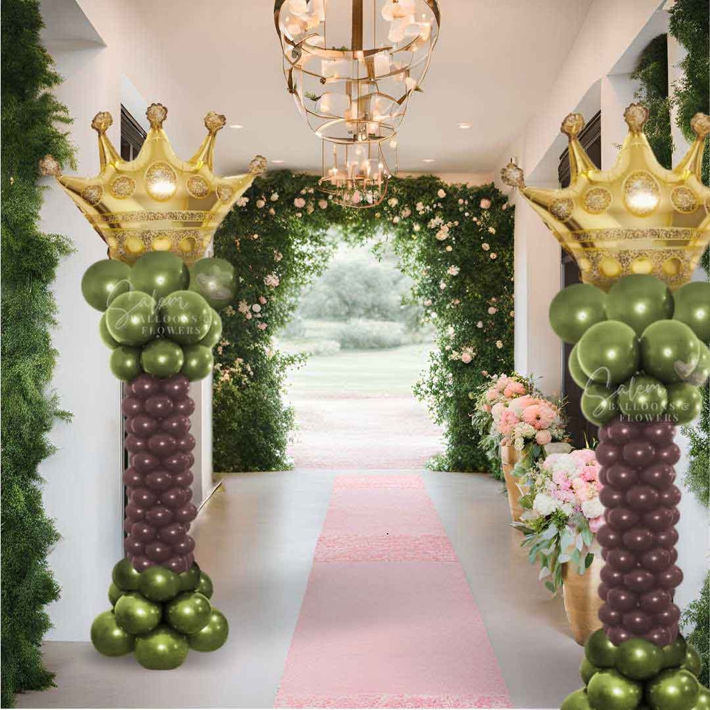 2 Balloon Columns in green and brown with a Golden Crown balloon topper standing in a hall with flowers. Oregon balloon decor.