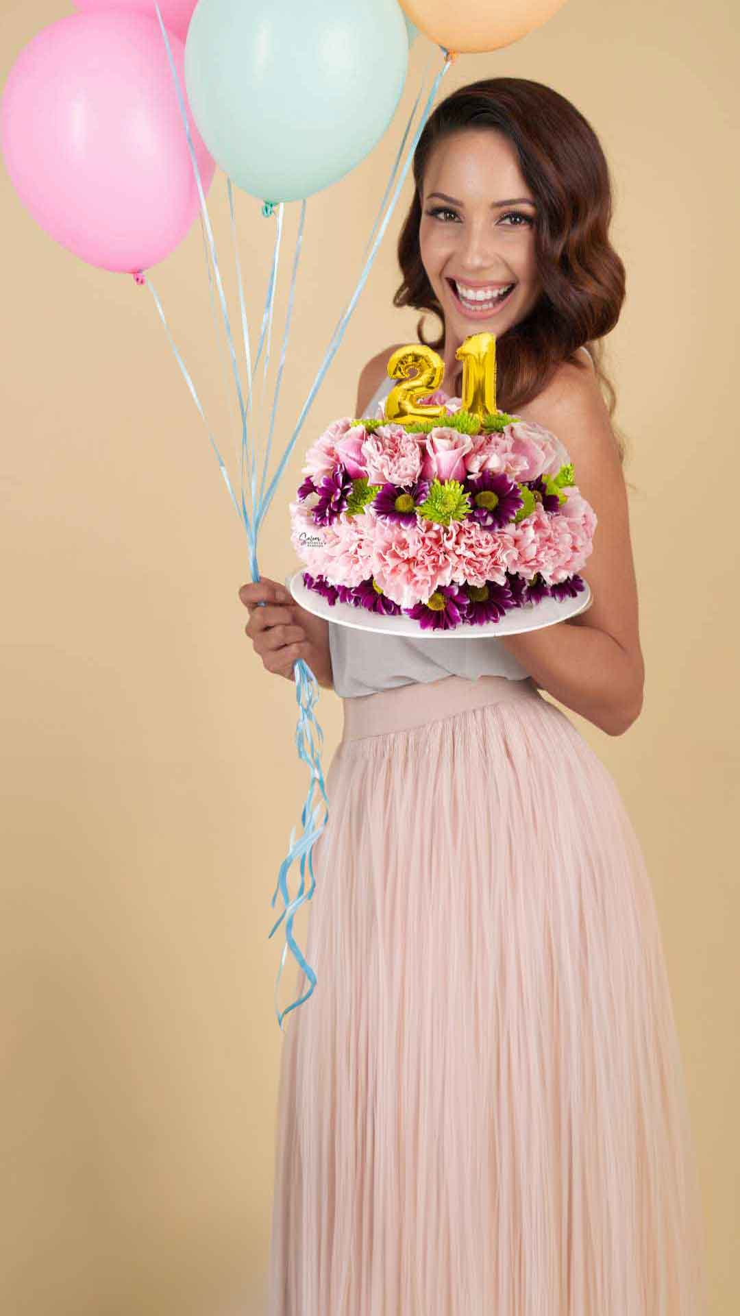 A young girl holding a cake shaped flower arrangement in one hand and balloons on the other hand. Salem Oregon flower delivery.