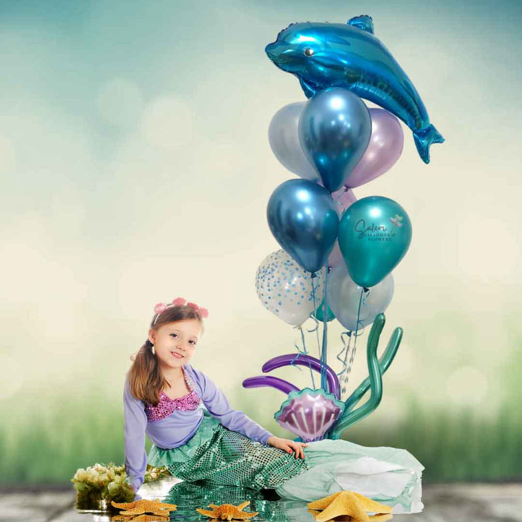 A little girl with a mermaid custom sitting next to a Under the Sea Helium Balloon Bouquet with a Blue dolphin balloon and seaweed balloons. Balloons Salem Oregon. 