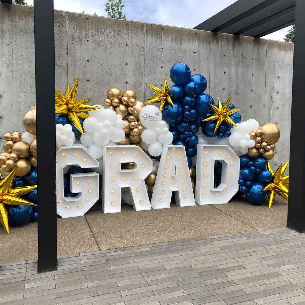 Front porch decorated with a Grad Balloon decor display. Featuring a GRAD light up marquee letters nested in a zaphire blue, gold and white balloon wall. Salem Oregon Balloon decor and marquee letters rental