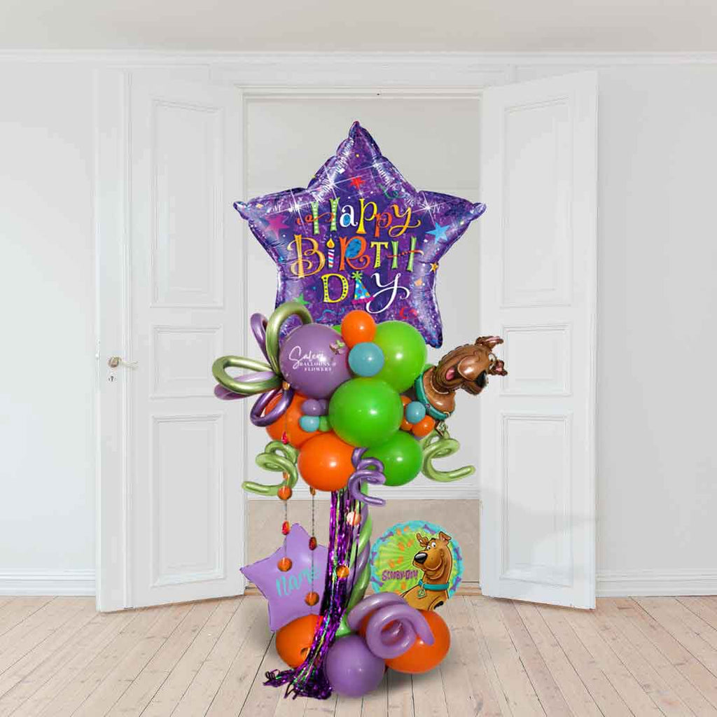 A Scooby Doo themed birthday balloon column in purple and orange standing in front of an open door. Approx 6 foot tall.  Salem Oregon Balloon Decor.