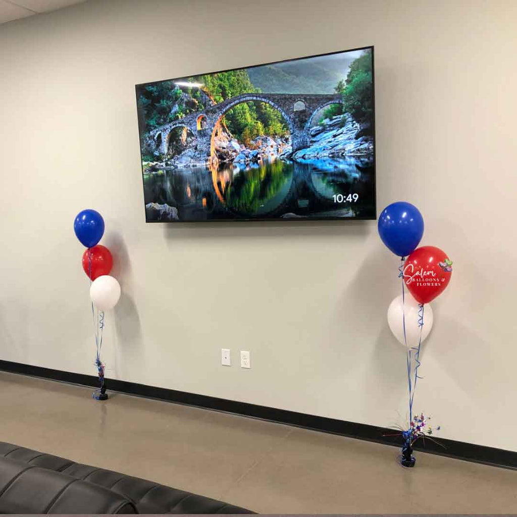 Wall with a large Tv decorated with 2 Balloon Centerpieces made of 3 helium balloons in red, white, and blue anchored to a decorated weight. Oregon Balloon Decor.