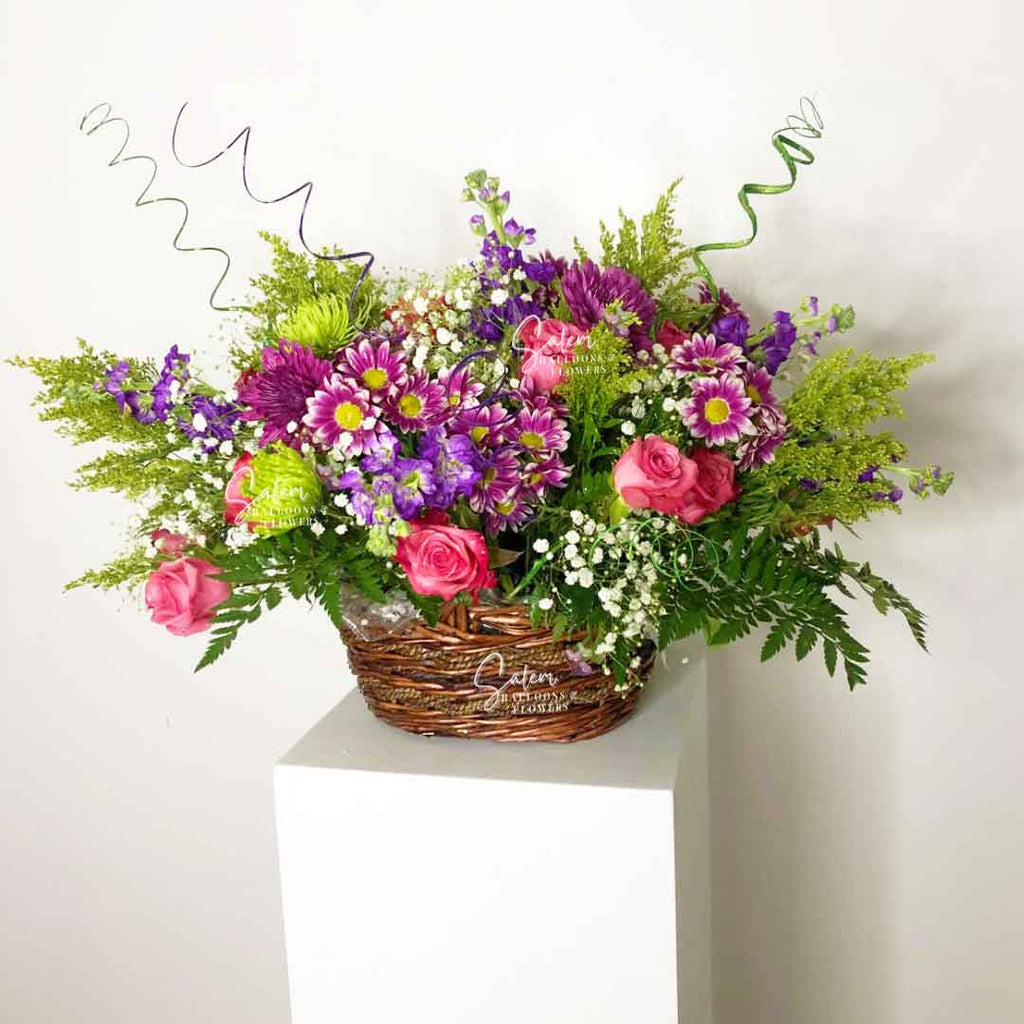 A A lavish flower arrangement, presented in a woven basket overflowing with fragrant blossoms, verdant foliage, and whimsical twigs standing on a white pedestal. Salem Oregon flower delivery.