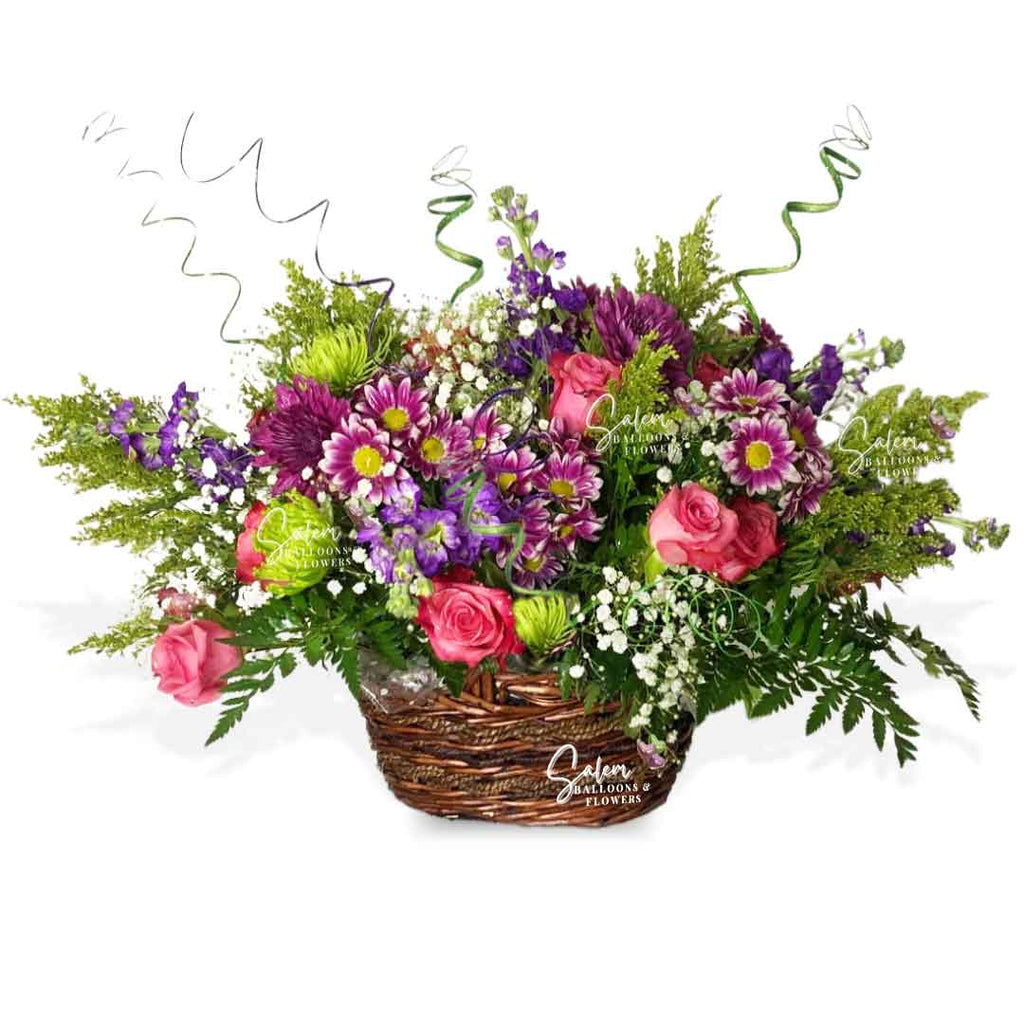 A lavish flower arrangement, presented in a woven basket overflowing with fragrant blossoms, verdant foliage, and whimsical twigs. Salem Oregon flower delivery.