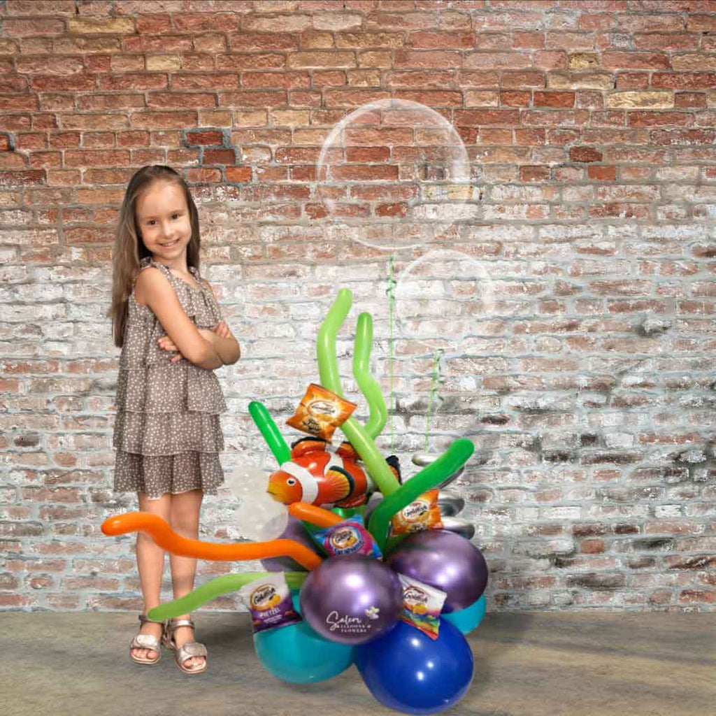 A little girl standing next to a  Nemo themed balloon bouquet a Nemo balloon swimming in a balloon reef surrounded by goldfish snacks as  2 large bubble balloons float above it standing in front of a brick wall. Salem Oregon balloon delivery.