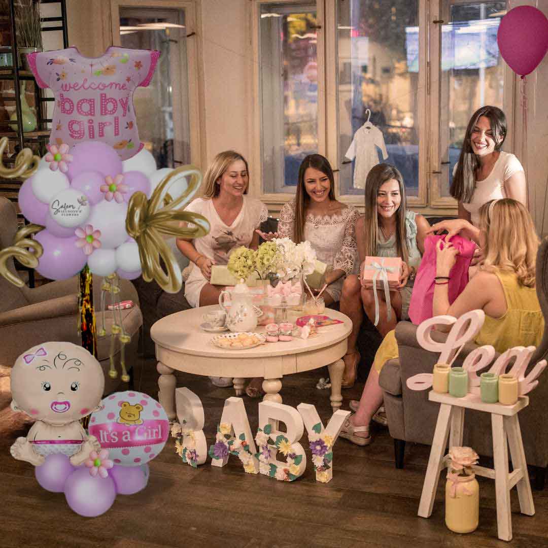 A group of ladies celebrating in a baby shower decorated with a Welcome baby girl balloon column, in pastel pink and white, and decorated with balloon flowers and curly balloons. Oregon Balloon Decor.