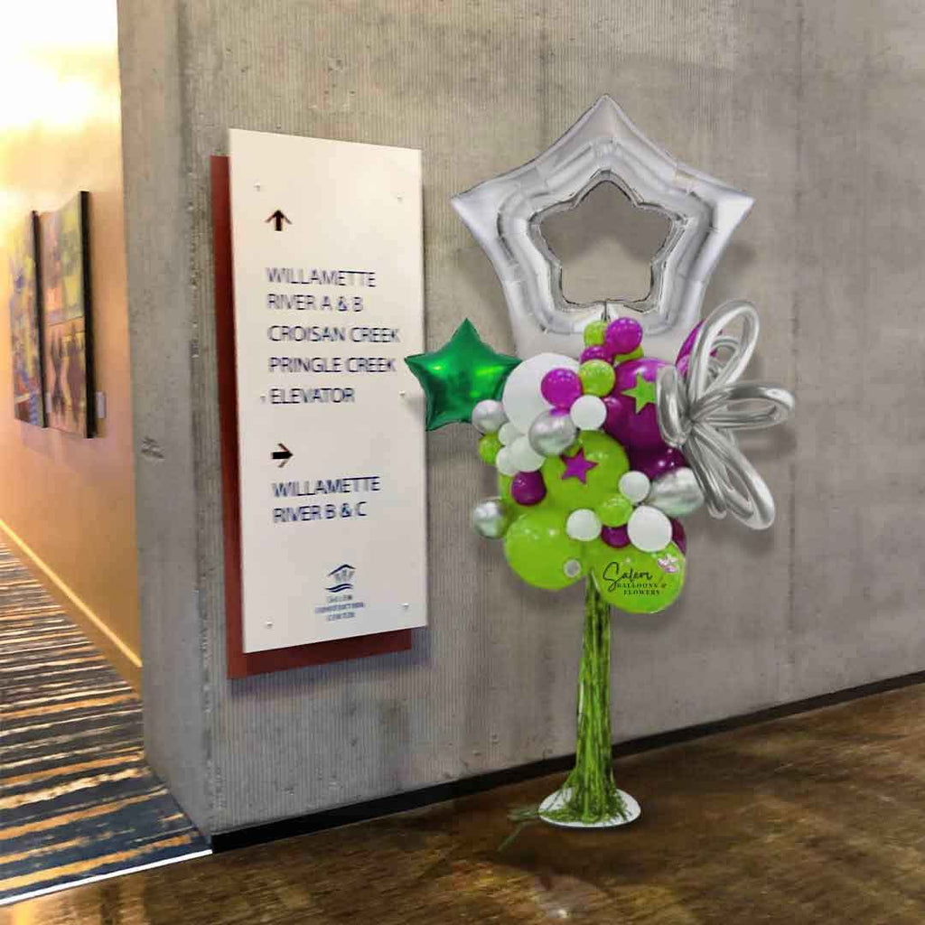 A Silver open Star Topper Balloon Column with tinsel bangs in various tones of green and magenta, decorated with curly balloons and stars, standing on a venue entrance. Oregon Balloon Decor.