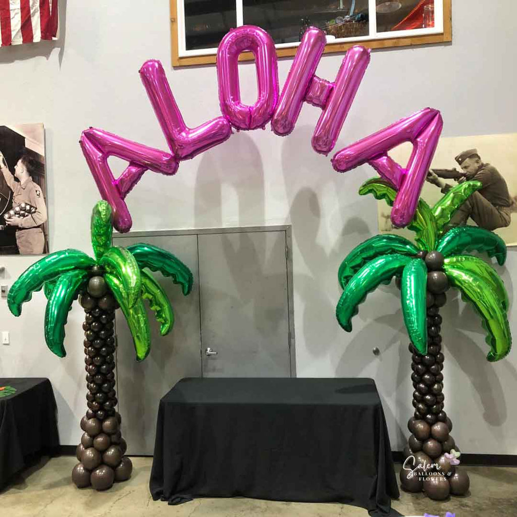 2 palm balloon columns with a pink ALOHA sign floating between them in a venue. Oregon Balloon Decor.