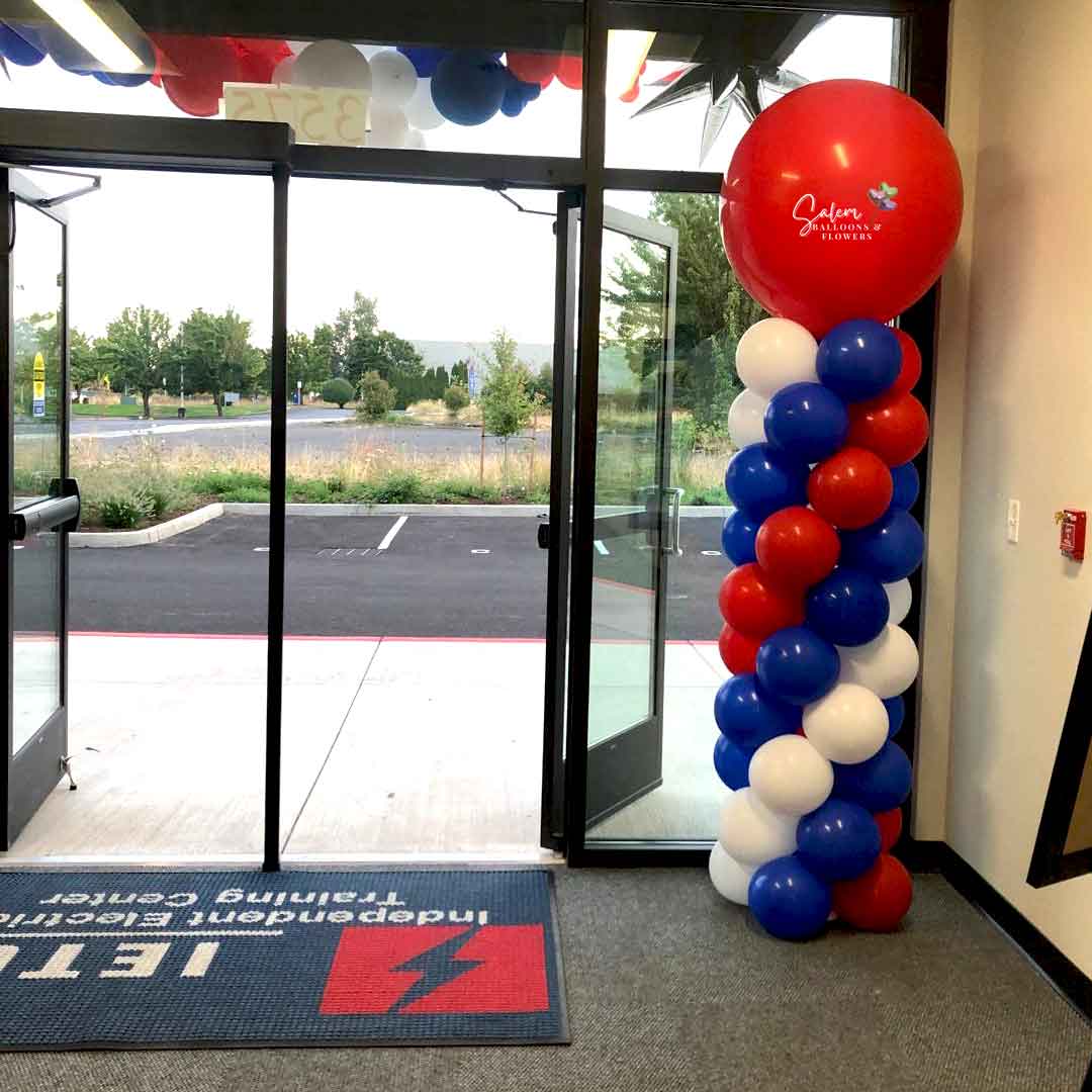 A Round top balloon column in a red, white and blue swirl standing on a main entrance. Oregon Balloon decor.