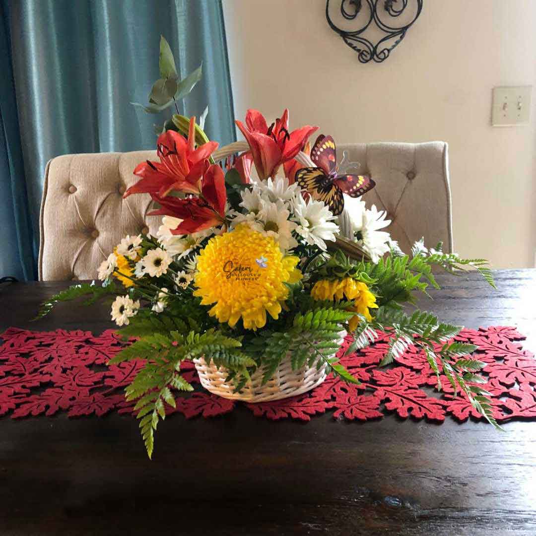 A Seasonal flower basket with an array of beautiful flowers decorated with butterflies sitting on a dining table. Salem Flower delivery.