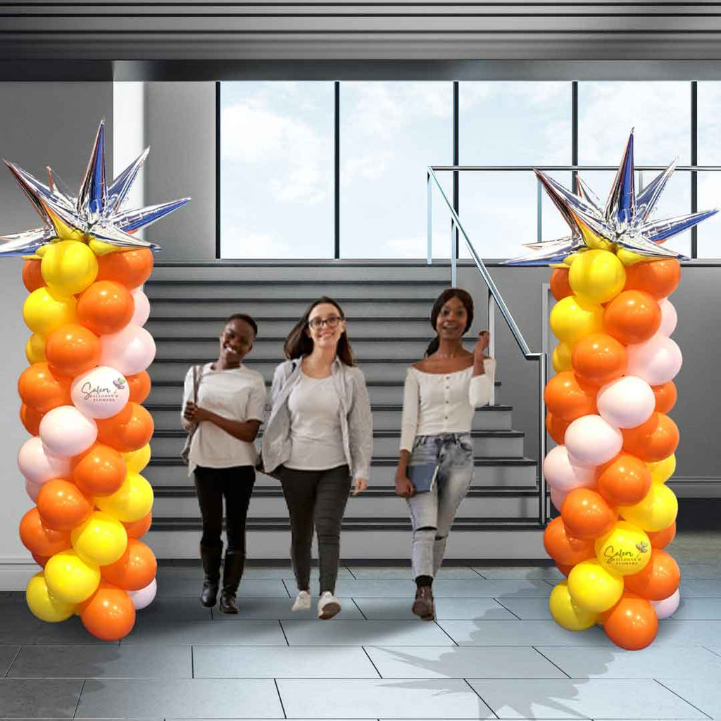 Two Classic balloon column with a silver starburst balloon topper. The body of the balloon column comes in a swirl of colors, standing side by side at the bottom of a staircase as students walk by. Salem Oregon Balloon decorations.