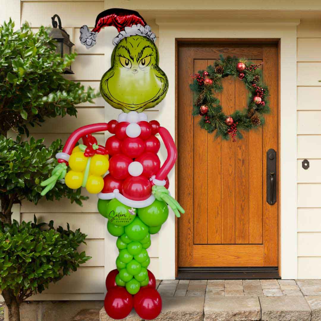 A Mr. Grinch Balloon column. Shaped as Mr. Grinch holding a gift. In a Green and red color palette standing in a front entry. Oregon Balloon Decortions