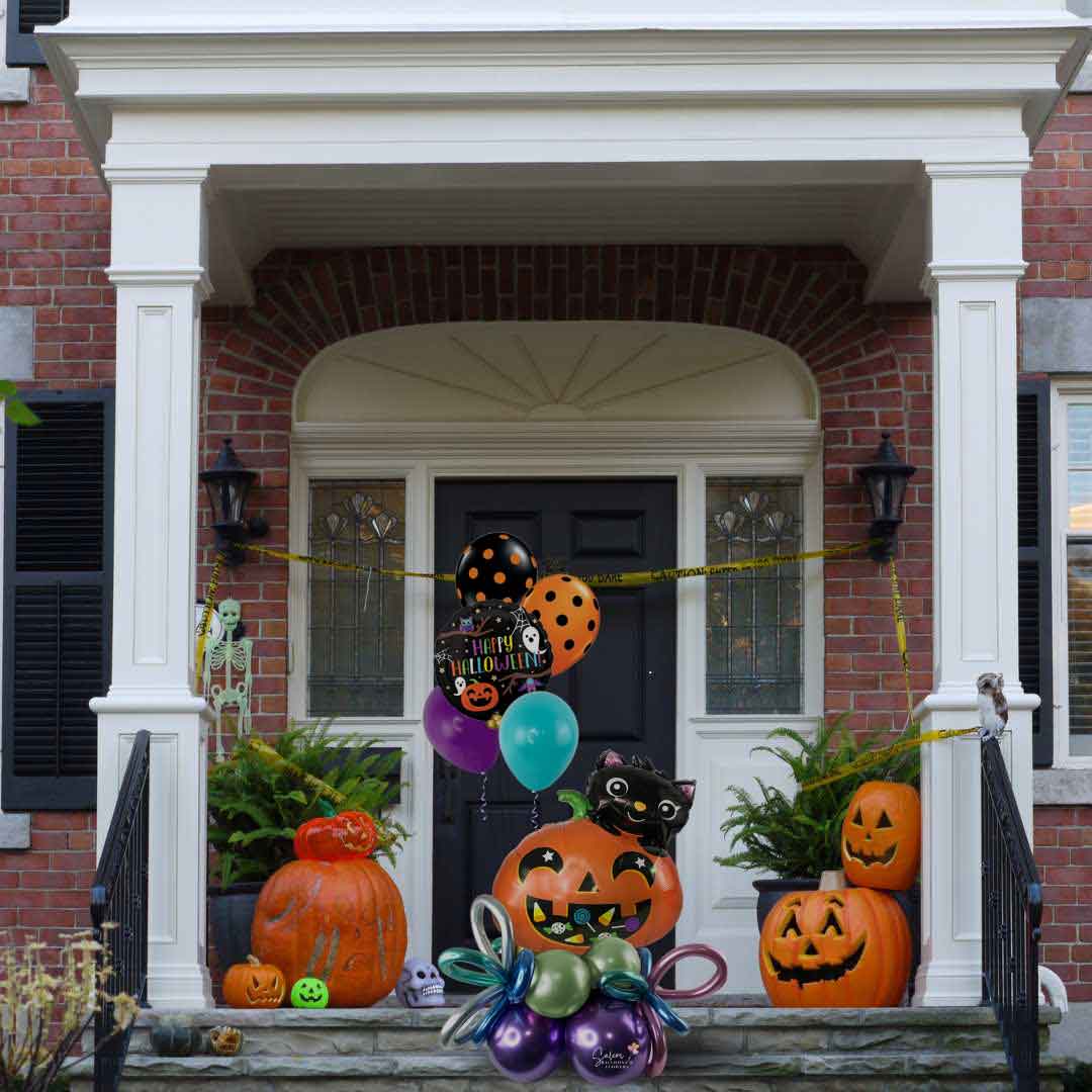 A Halloween themed balloon bouquet, featuring a pumpkin balloon with a cute black cat, decorated with helium balloons and curly balloons standing on a front porch. Oregon Balloon delivery.