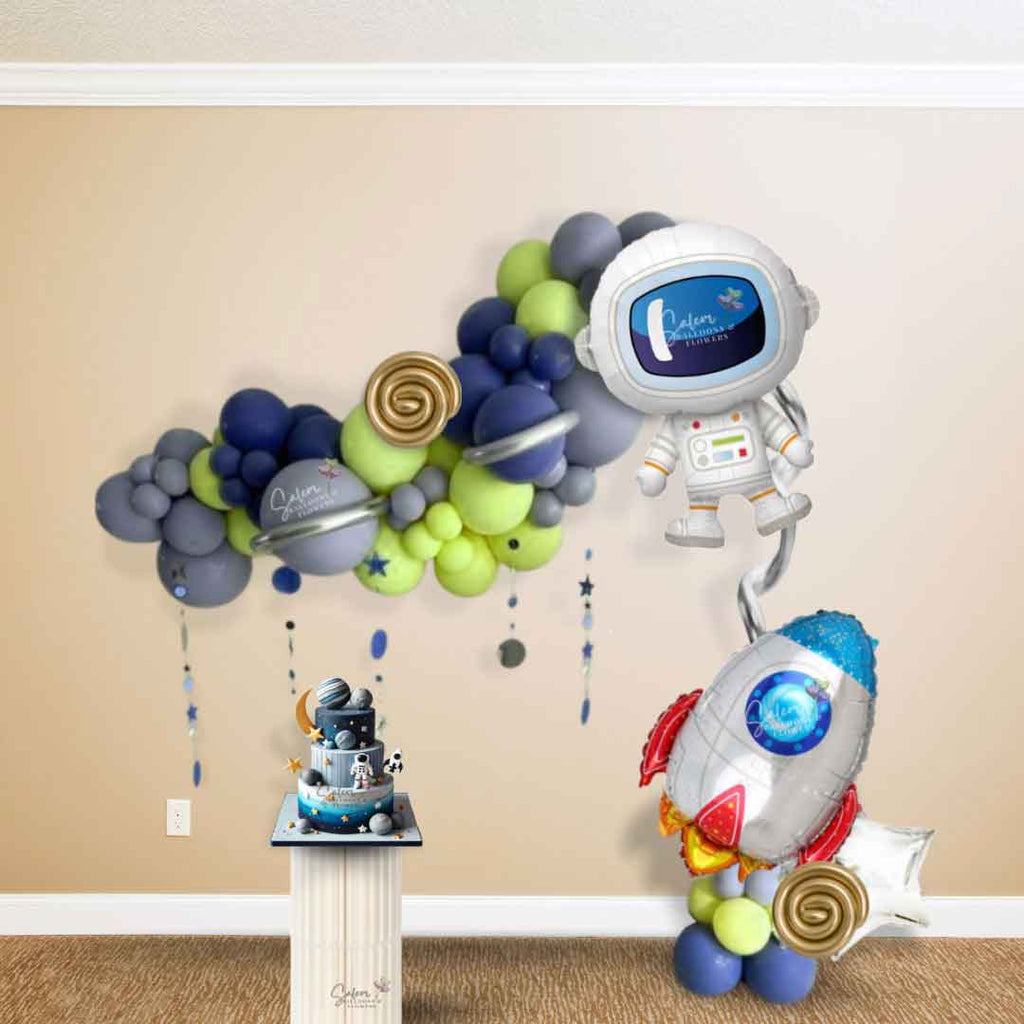 Space-themed balloon decor in silver, dusk blue, and navy blue, showcasing an 8-foot organic garland adorned with an astronaut foil balloon, star and planet accents, and a rocket-themed satellite balloon arrangement. Perfect for events in Salem, Oregon, and surrounding areas.