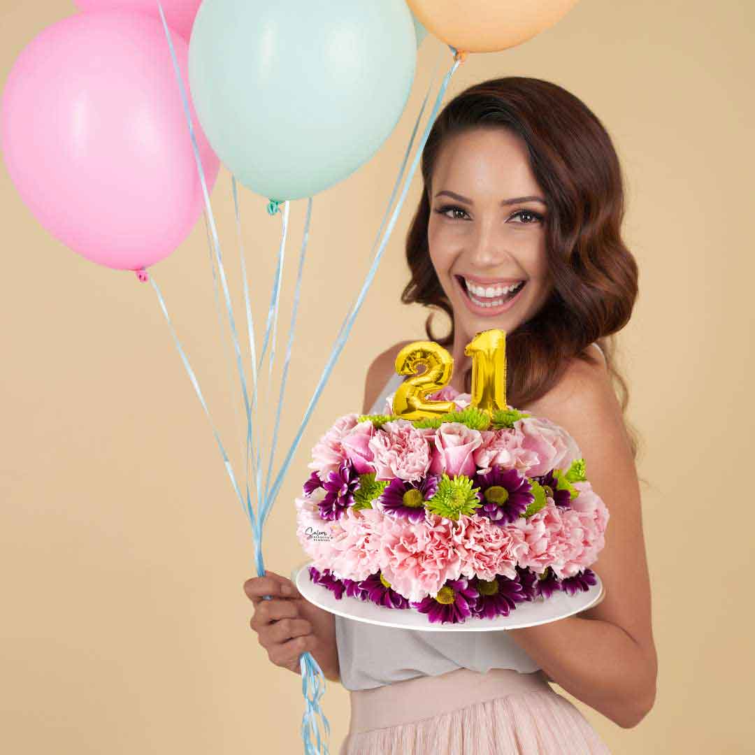 A young girl holding a cake shaped flower arrangement in one hand and balloons on the other hand. Salem Oregon flower delivery.