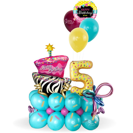 Happy Birthday, balloon bouquet. Featuring a giant gorgeous and funky cake and donuts-shaped balloon numbers on a balloon base decorated with sprinkles and whimsical colorful balloons.