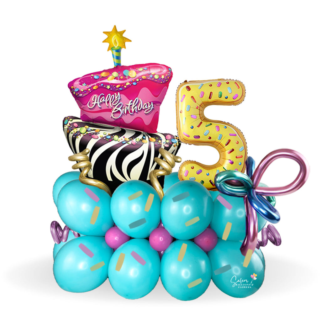 Happy Birthday, balloon bouquet. Featuring a giant gorgeous and funky cake and donuts-shaped balloon numbers on a balloon base decorated with sprinkles and whimsical colorful balloons.